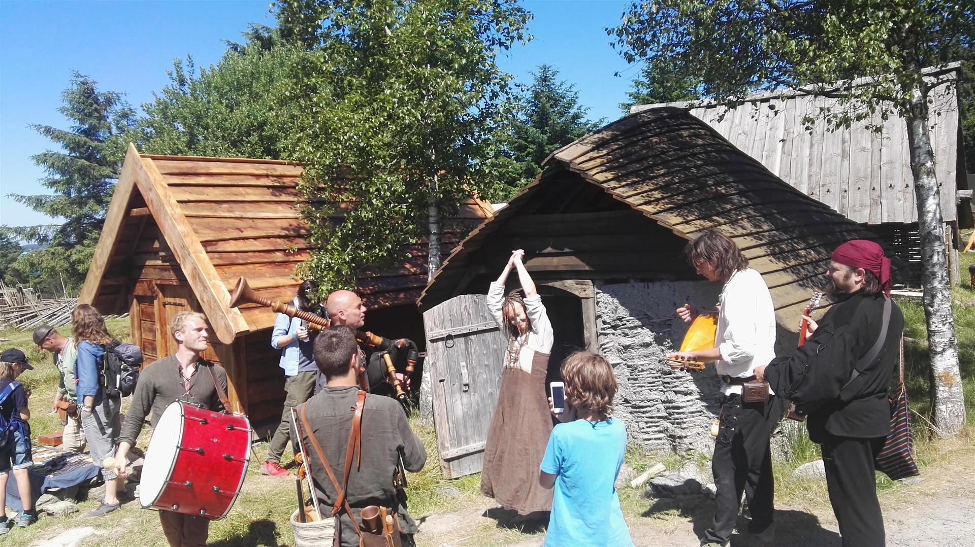 Vikinger som danser og spiller musikk foran gropehus på vikingfestivalen